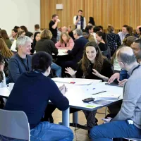 Students, academics, and external partners in group discussions around tables
