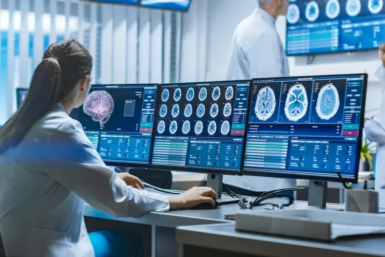 Medical professional analyzing brain scans on multiple computer monitors in a modern lab, representing medical imaging and diagnostics