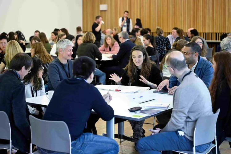Students, academics, and external partners in group discussions around tables